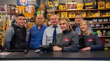 Howdens depot staff members, in branch behind a counter. They are wearing branded workwear.