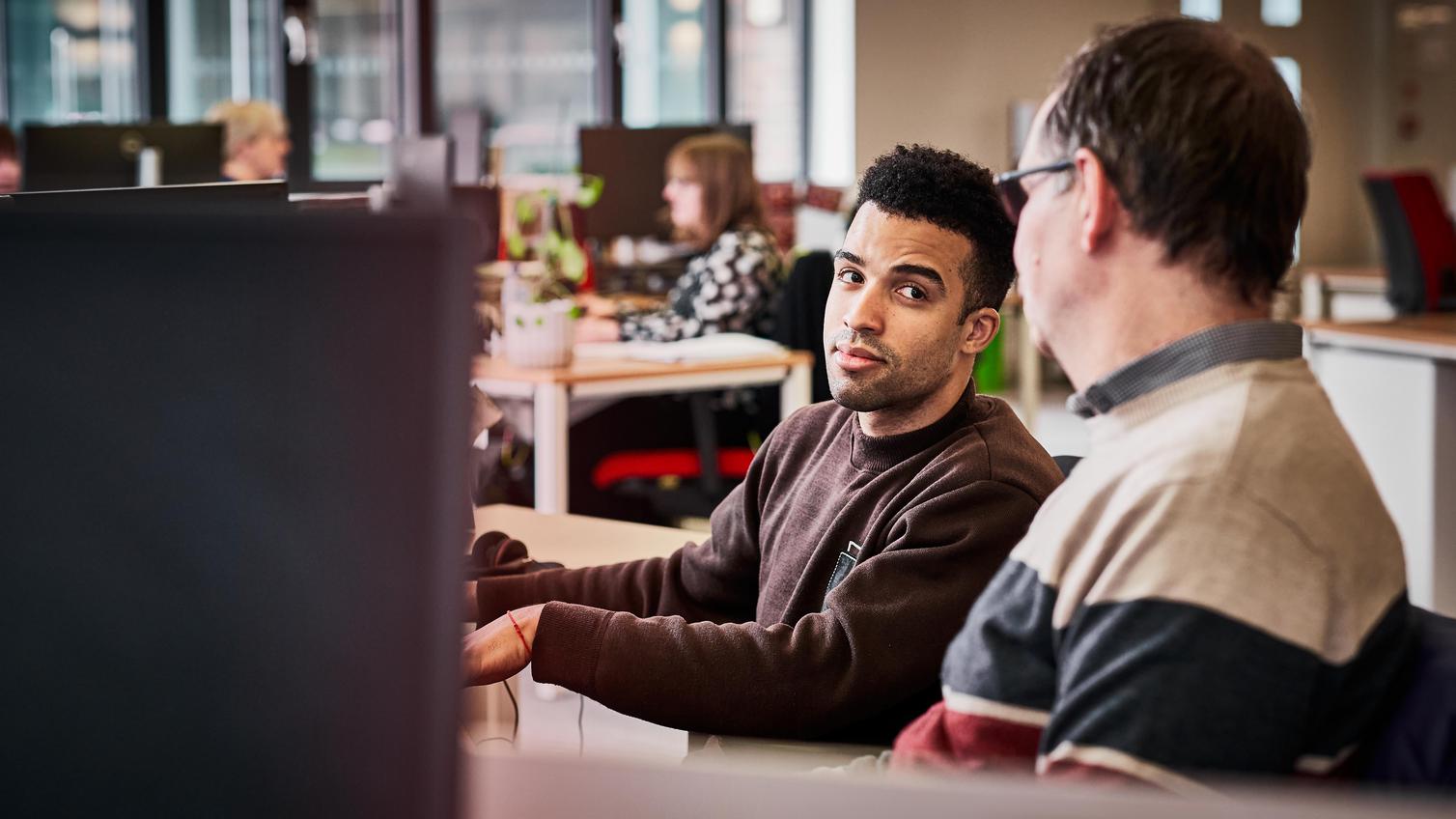 Two Howdens support staff in an office setting, sat at a desktop using a computer.