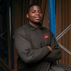 Image of an apprentice warehouse worker, standing in the depot smiling at the camera
