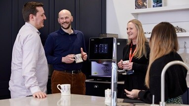 4 people stood in a kitchen, 2 men on the left, 2 women on the right, chatting and smiling