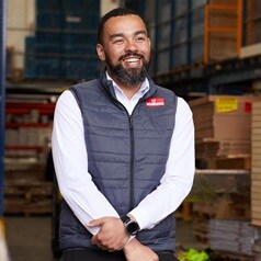 A Howdens depot manager, stood in the warehouse with various stock and shelving behind them.