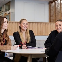 Four members of Howdens office staff, sat at a desk, discussing Howdens reward and benefits.