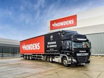 Howdens delivery lorry, featuring large logo and royal warrant seal, in an industrial car park.